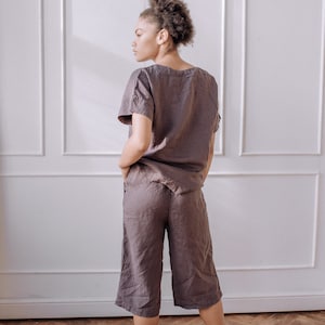 May include: A woman wearing a dark grey linen short-sleeved top and matching linen trousers. The trousers are cropped and have a wide leg.
