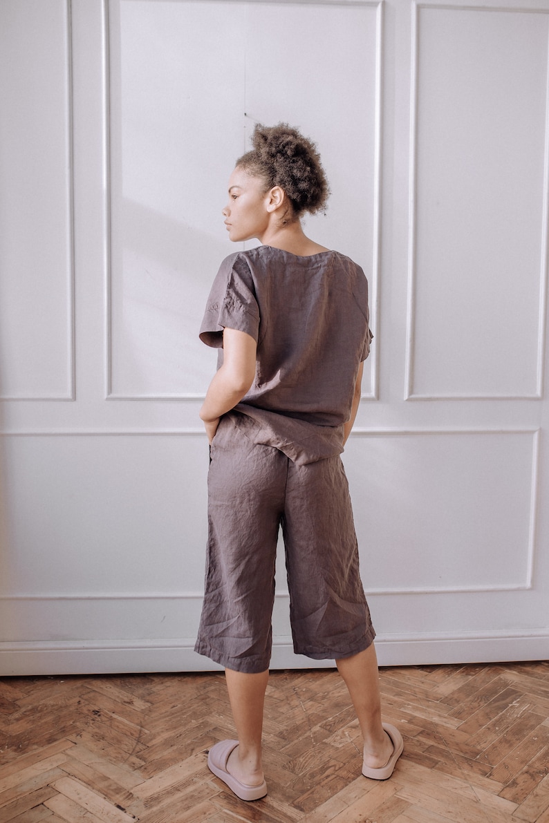 May include: A woman wearing a dark grey linen short-sleeved top and matching linen trousers. The trousers are cropped and have a wide leg.
