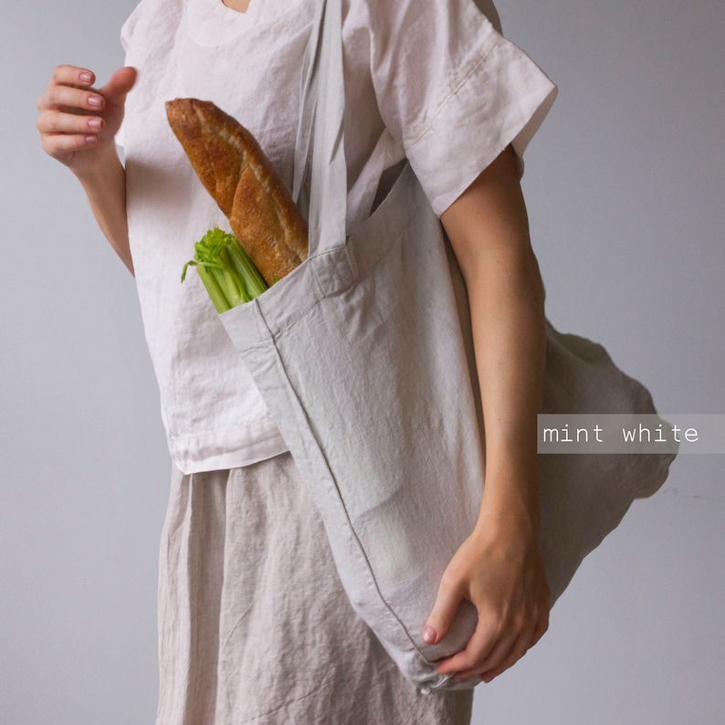 May include: A light gray tote bag filled with a baguette and celery. The bag is made of a soft, textured fabric and has long straps. The text "mint white" is visible in the bottom right corner.