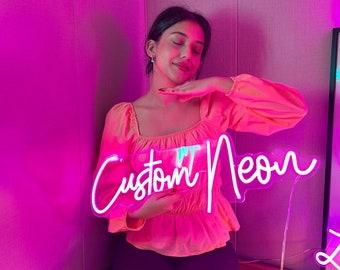 May include: A bright white neon sign featuring the text Custom Neon in a cursive script font. The sign is mounted on a clear acrylic backing and emits a vibrant glow, illuminating the surrounding area with a distinct light.