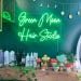 May include: Green Moon Hair Studio neon sign with white lettering on a green wall. The sign is lit up and there are several bottles of hair products on a shelf below the sign.