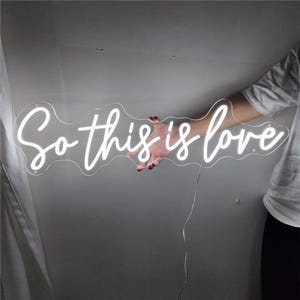 May include: White neon sign with the text "So this is love" in a cursive font.