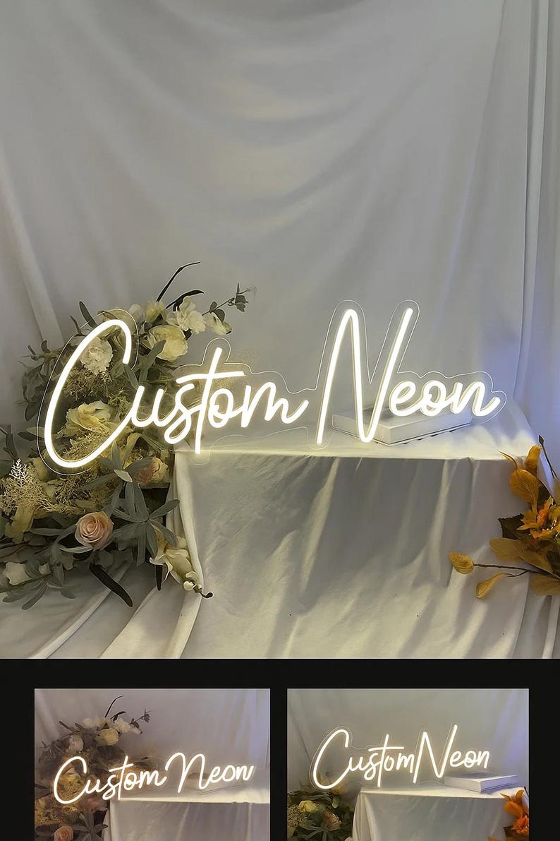 May include: A custom neon sign featuring the words Custom Neon in a white glowing script font. The sign is mounted on a clear acrylic backing and is displayed alongside floral arrangements with white and yellow flowers on a draped white fabric.