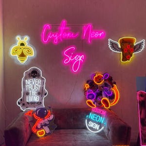May include: A collection of neon signs with various designs, including a bee, a tombstone with the text "Never Trust the Living", a pizza with wings, a cartoon astronaut, and the text "Custom Neon Sign".