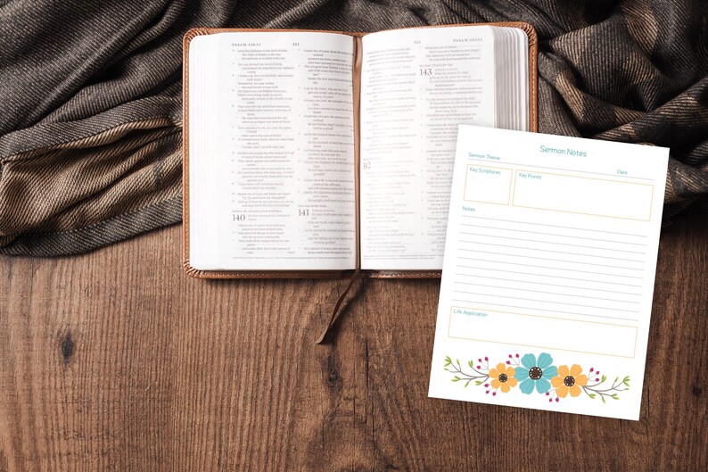 Puede incluir: Una Biblia abierta con una cubierta de cuero marr&oacute;n y un marcador a juego descansa sobre una superficie de madera. Un bloc de notas con las palabras "Notas del serm&oacute;n" y un dise&ntilde;o floral est&aacute; al lado de la Biblia. Una tela marr&oacute;n y gris est&aacute; drapeada en el fondo.