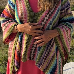 Puede incluir: Un poncho de punto de rayas de colores con cuello en V y un patrón geométrico. El poncho está hecho de un hilo suave y cálido y es perfecto para capas en los meses más fríos.