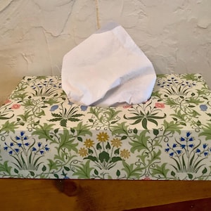 May include: A tissue box cover with a floral pattern in shades of green, blue, yellow, and pink. The cover features a repeating design of leaves, flowers, and vines.