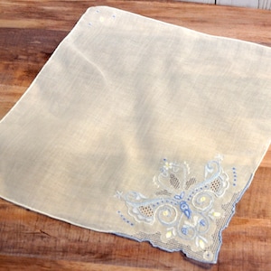 May include: A white handkerchief with blue and yellow embroidered floral design. The embroidery features a butterfly design.