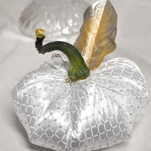 May include: A white fabric pumpkin with a silver glitter pattern and a green stem with a gold leaf.