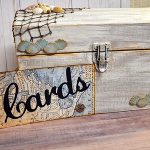 May include: A white wooden box with a nautical theme, decorated with seashells, a net, and a seahorse. The box has a label that says "cards" and is perfect for holding wedding cards or other special occasion cards.