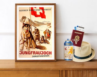 Może przedstawiać: Oprawiony plakat podróżniczy w stylu vintage przedstawiający trzy psy zaprzęgowe na pierwszym planie, szwajcarską flagę, ośnieżone góry i ludzi w tle z napisem BERNER OBERLAND SCHWEIZ oraz JUNGFRAUJOCH JUNGFRAUBAHN. Obok znajduje się niebieska puszka, paszport i słomkowy kapelusz.