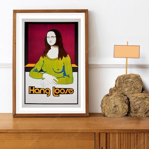 May include: A framed art print featuring a pop art interpretation of the Mona Lisa. The artwork depicts the subject in a green top with the text "Hang Loose" in orange and black. The frame is brown.