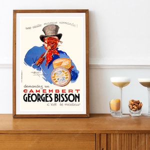 May include: A framed vintage advertisement poster featuring a smiling person in a top hat and blue coat holding a knife and a round box of Camembert Georges Bisson cheese. The text reads: une vieille marque normande! demandez un CAMEMBERT GEORGES BISSON c'est le meilleur.
