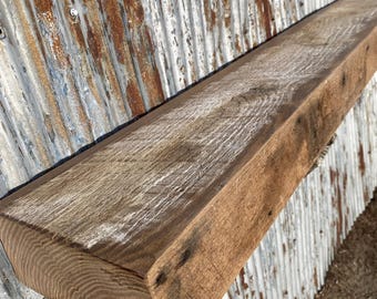 May include: A rustic, rectangular wooden beam with a natural, weathered appearance. The beam is a warm brown color with visible wood grain and some white paint remnants. The end of the beam is rounded. The background is a corrugated metal surface.