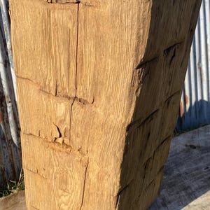 May include: A large, solid, rectangular wooden block with a natural, light brown finish. The wood grain is visible, and the block has a rough, textured surface with visible cracks and imperfections. The block is likely a decorative or functional item.