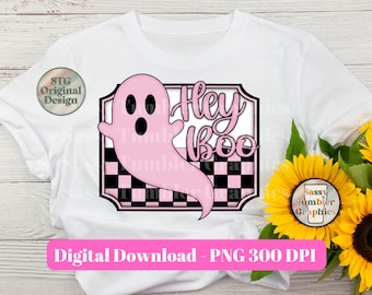 May include: White t-shirt featuring a pink ghost graphic with the words "Hey Boo" in a playful font. The design includes a black and white checkered pattern. The image also includes sunflowers.