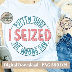 Puede incluir: Una camiseta blanca con un gráfico circular turquesa que dice "Pretty Sure I Seized the Wrong Day". El gráfico tiene un contorno rosa y las palabras "Pretty Sure" y "the Wrong Day" están en turquesa. Las palabras "I Seized" están en rosa. La camiseta está sobre una superficie de madera con un par de zapatillas grises, unos vaqueros azules y unos auriculares.