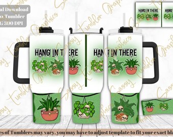 May include: A 40oz tumbler with a black handle and a white lid. The design features the text "HANG IN THERE" above illustrations of potted plants and skulls. The bottom of the tumbler has a green background with more plant and skull designs.