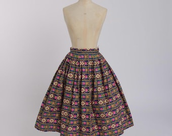 May include: A vintage knee-length skirt with a vibrant floral and geometric pattern. The skirt features a navy blue background with pink, yellow, and white floral and geometric designs. The skirt is displayed on a mannequin.