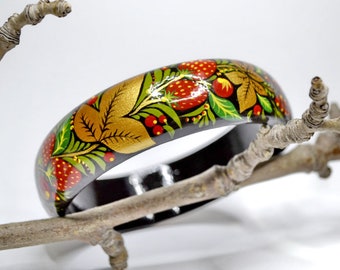 May include: A wooden bangle painted with a traditional Russian folk art design. The design features red berries, green leaves, and gold accents on a black background.