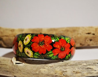 May include: A black wooden bangle with a floral design. The flowers are red, yellow, and green. The bangle is painted with a black background.