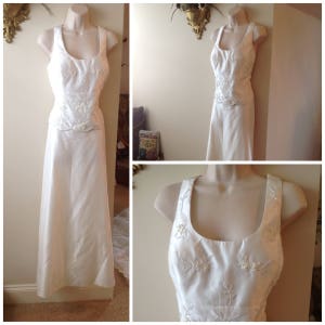 May include: A white two-piece wedding dress with a beaded bodice and a flowing skirt.