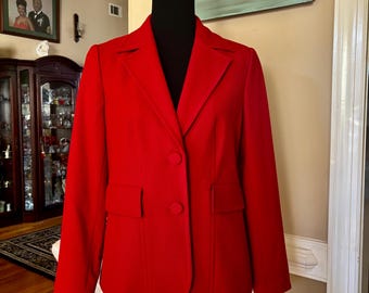 May include: A vibrant red blazer with a classic two-button closure and two front pockets. The blazer is displayed on a black mannequin, showcasing its tailored fit and structured design. The jacket's bold color makes it a statement piece.
