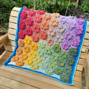 May include: A colorful crochet blanket with a honeycomb pattern featuring a variety of flower designs in shades of red, orange, yellow, green, blue, and purple.