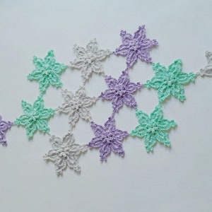 May include: A crocheted garland with a repeating pattern of six-pointed stars in shades of light green, lavender, and gray.