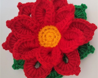 May include: A red crocheted poinsettia flower with a yellow center and green leaves.