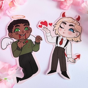 May include: Two cartoon characters, one with a halo and wings and the other with horns and a tail, are depicted in a playful, contrasting style. The angel character has green eyes and brown skin, while the devil character has blue eyes and fair skin. Both characters are wearing clothing and have a heart-shaped object in their hands.