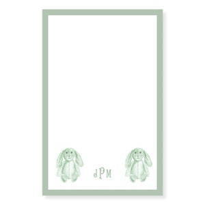 Può includere: Un bordo verde circonda uno sfondo bianco con due illustrazioni di conigli verdi e il monogramma "JPM" al centro.