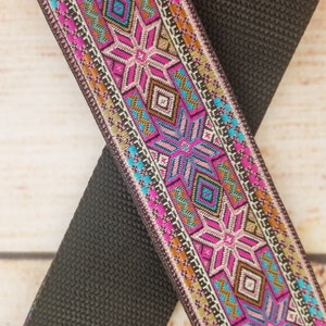 May include: Black and pink patterned woven ribbon with a geometric design. The ribbon is woven with a variety of colors, including black, pink, turquoise, gold, and white.