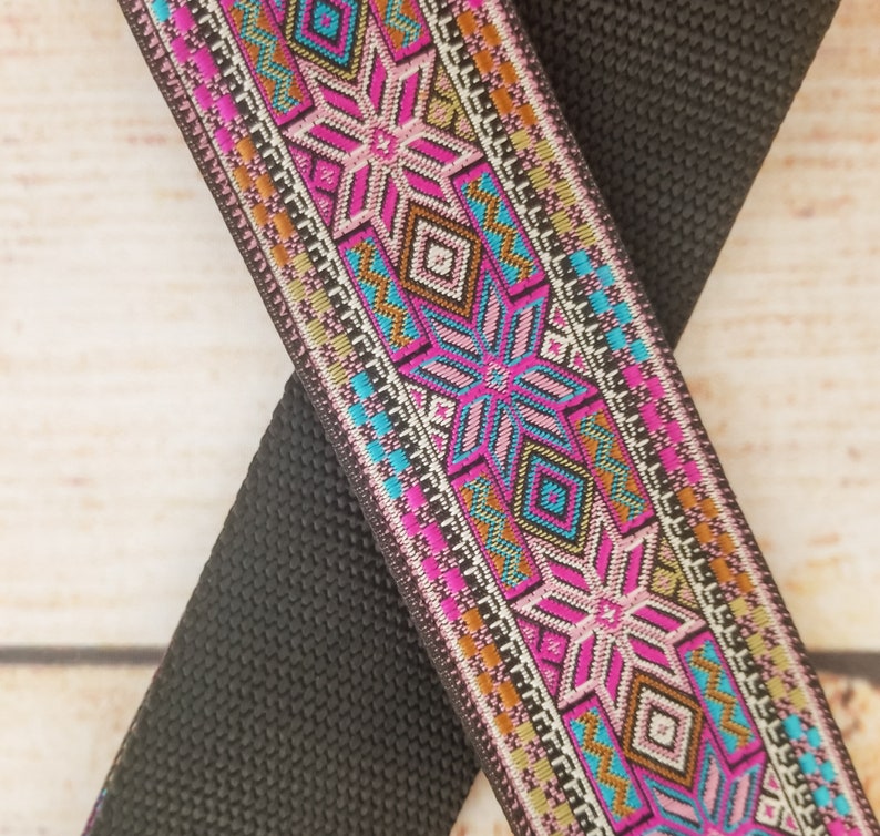 May include: Black and pink patterned woven ribbon with a geometric design. The ribbon is woven with a variety of colors, including black, pink, turquoise, gold, and white.