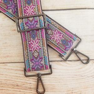 May include: Two colorful patterned fabric straps with silver metal clasps. The straps have a geometric design with pink, blue, and gold accents.