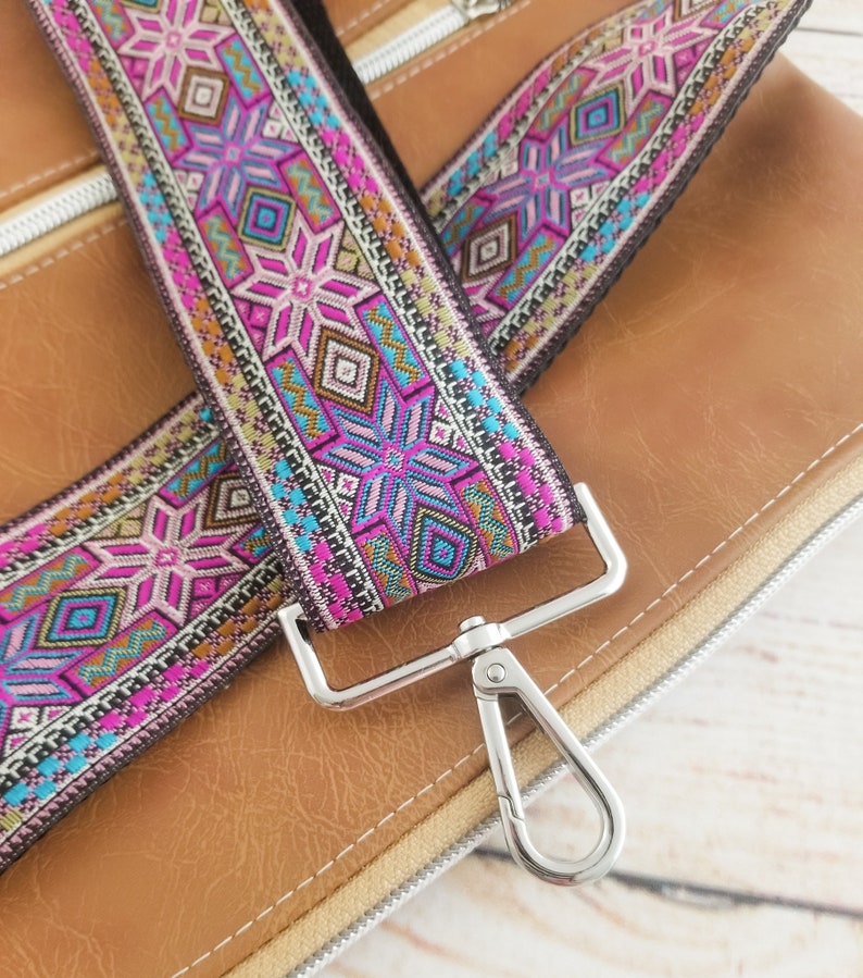 May include: A close-up of a brown leather bag with a colorful patterned strap and a silver swivel clasp.