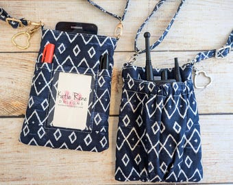 May include: Two navy blue and white patterned crossbody phone pouches with adjustable straps. One pouch holds a phone, pens, and a card with the text "Katie Rene Designs". The other pouch holds a radio and other accessories. Both have gold-colored hardware.