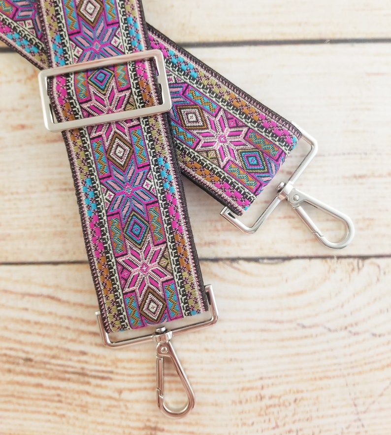 May include: A pair of colorful patterned adjustable straps with silver metal clasps. The straps are made of woven fabric with a geometric design in shades of pink, blue, brown, and gold.