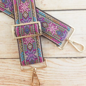 May include: A pair of colorful patterned fabric straps with gold metal clasps and swivel hooks. The straps have a geometric design with pink, blue, and gold accents.