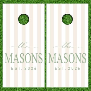Könnte beinhalten: Zwei rechteckige Cornhole-Boards mit einem vertikalen Streifenmuster in Weiß und Hellbeige. Jedes Board hat oben ein kreisförmiges Loch und zeigt den Text "the MASONS" in Salbeigrün mit dem darunter gedruckten "EST. 2026".