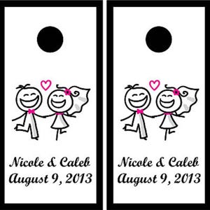 May include: Two white rectangular cornhole boards with black borders and a circular hole at the top. Each board features a stick figure couple illustration with pink accents, the text Nicole & Caleb, and the date August 9, 2013 in black script.