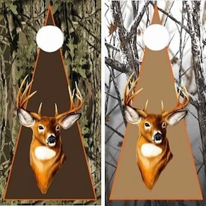 May include: Two rectangular cornhole boards featuring a deer head graphic centered on a triangular background. The left board displays a green forest camouflage pattern, while the right board features a white and gray winter tree camouflage design.