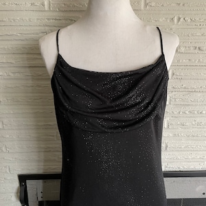 May include: A black spaghetti strap dress with a cowl neck and a sparkly texture.