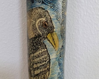 May include: A wooden walking stick with a hand-painted design of a bird and swirling clouds. The bird has a yellow beak and black and white feathers. The clouds are blue and white.