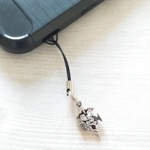 May include: A black phone with a silver charm attached to it. The charm is a stylized medical symbol with a snake wrapped around a staff.