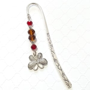 May include: Silver bookmark with a floral design and a silver butterfly charm. The bookmark is decorated with red and brown glass beads.