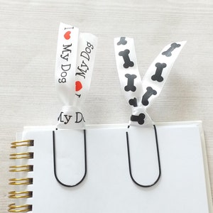 May include: Two white ribbon bookmarks with black clip holders. One bookmark has a black and white bone print and the other says "I love my dog" with a red heart.