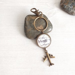 May include: A bronze keychain with a round charm that says "Let the Adventure Begin" and a small airplane charm.
