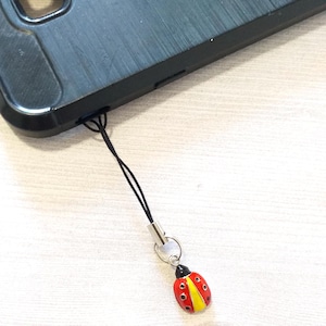 May include: A black phone with a black and red ladybug phone charm attached to it.