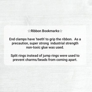 May include: A white card with black text describing the features of ribbon bookmarks. The text reads: "Ribbon Bookmarks. End clamps have 'teeth' to grip the ribbon. As a precaution, super strong industrial strength non-toxic glue was used. Split rings instead of jump rings were used to prevent charms/beads from coming apart."